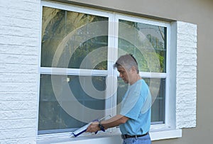 Homeowner caulking window weatherproofing home against rain water and storms photo