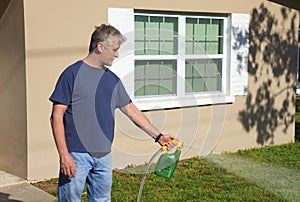 Homeowner man spraying weed killer on the grass in his yard with hose attachment full of chemicals photo