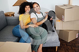 Homeowner, portrait and lesbian couple with a dog on the sofa for moving boxes and a new home. Smile, lgbt and women or