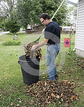 Homeowner Putting Leaves In A Trash Carrel