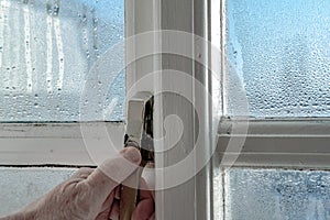 Homeowner seen unlocking a wooden framed window during a cold morning.