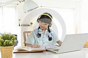 Homeschool Asian little young girl student learning virtual internet online class on table at home