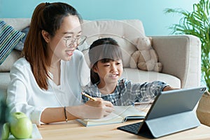 Homeschooling. Asian family with daughter doing homework by using tablet with mother help. Asia mom and child learning online with