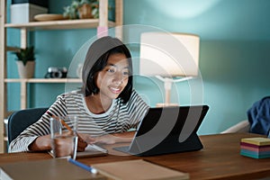 Homeschooling Asian girl doing homework And study online with tutor on tablet at desk at night photo