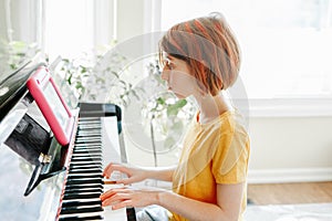 Homeschooling for children. Girl learning to play piano in virtual online school class on digital tablet. Kid playing music at photo