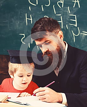 Homeschooling concept. Father checking homework, helps to boy, son. Teacher in formal wear and pupil in mortarboard in