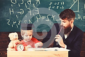 Hometask concept. Father checking hometask, helps to boy, son. Teacher in formal wear and pupil in mortarboard in