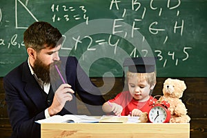 Hometask concept. Father checking hometask, helps to boy, son. Teacher in formal wear and pupil in mortarboard in
