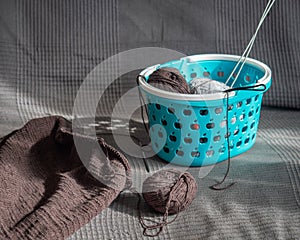 Homework, making knitted items from brown cotton yarn, a blue basket with balls of yarn on a sofa