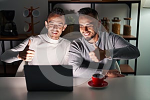 Homosexual couple using computer laptop approving doing positive gesture with hand, thumbs up smiling and happy for success