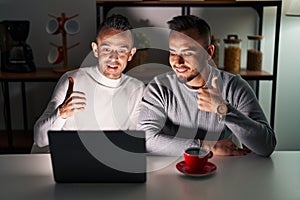 Homosexual couple using computer laptop doing happy thumbs up gesture with hand