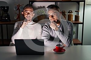 Homosexual couple using computer laptop with hand on chin thinking about question, pensive expression