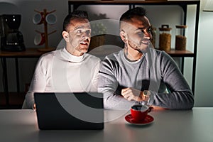 Homosexual couple using computer laptop looking away to side with smile on face, natural expression