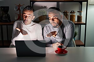 Homosexual couple using computer laptop looking at the camera blowing a kiss with hand on air being lovely and sexy