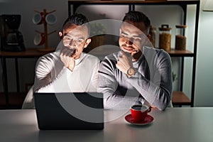 Homosexual couple using computer laptop looking confident at the camera smiling with crossed arms and hand raised on chin