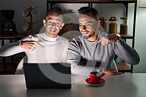 Homosexual couple using computer laptop looking confident with smile on face, pointing oneself with fingers proud and happy