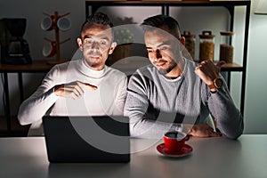 Homosexual couple using computer laptop pointing to the back behind with hand and thumbs up, smiling confident