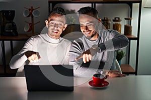 Homosexual couple using computer laptop pointing to you and the camera with fingers, smiling positive and cheerful