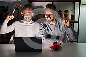 Homosexual couple using computer laptop smiling amazed and surprised and pointing up with fingers and raised arms