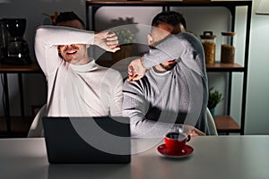 Homosexual couple using computer laptop smiling cheerful playing peek a boo with hands showing face