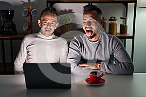 Homosexual couple using computer laptop sticking tongue out happy with funny expression