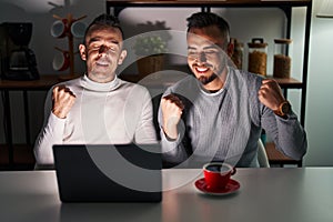 Homosexual couple using computer laptop very happy and excited doing winner gesture with arms raised, smiling and screaming for