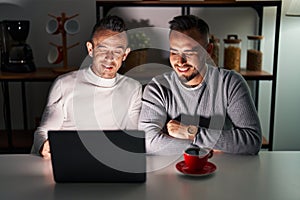 Homosexual couple using computer laptop winking looking at the camera with sexy expression, cheerful and happy face