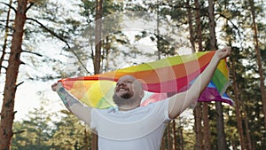 Homosexual man running with rainbow gay flag in forest park. Happy guy demonstrate his rights. Shameless queer showing