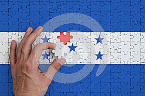 Honduras flag is depicted on a puzzle, which the man`s hand completes to fold