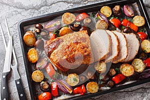 Honey baked pork loin with potatoes, onions, bell peppers and mushrooms close-up on a baking sheet. Horizontal top view