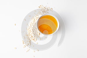 Honey in a bowl with scattered oat flakes on a white background