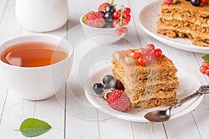Honey cake with strawberries, mint and currant, a Cup of tea on a light background