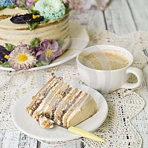 Honey cake on a white table with cup of coffe. Cake with cream flowers. Close up, copy space.