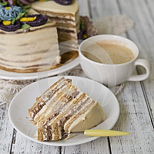 Honey cake on a white table with cup of coffe. Cake with cream flowers. Close up, copy space.