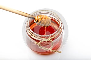 Honey in a clear glass jar There is a wooden dipper that stirs honey and drops honey