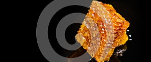 Honey close-up. Amber sweet honey in honeycomb. Square cut piece of honeycomb with honey on a black background
