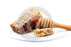Honey comb in a platel and wooden stick.