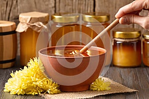 Honey with a dipper in a clay bowl and flowers on a dark wooden background