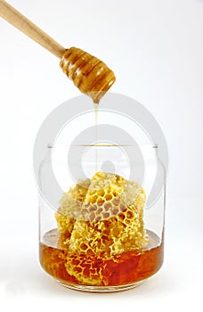 Honey dipper with fresh honey and honeycomb in glass jar