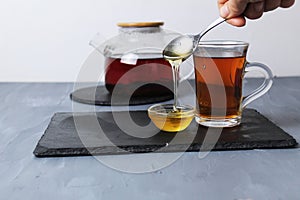 Honey drains from the spoon in a thin stream. Honey and tea treatment folk remedies for colds. Teapot tea in a glass and honey on