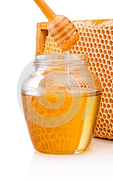 Honey dripping from dipper into glass jar on background honeycomb
