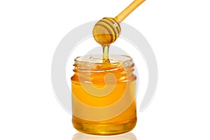 Honey dripping from honey dipper into glass jar isolated on white. Close-up. Healthy organic thick honey