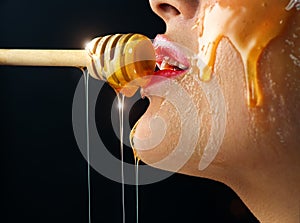 Honey dripping from honey dipper on sexy girl lips. Thick honey dipping from the wooden honey spoon. Beauty model woman