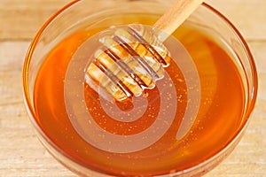 Honey dripping from honey dipper in glass bowl. Thick honey dipping from the wooden honey spoon, closeup.