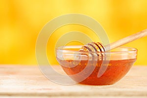 Honey dripping from honey dipper in glass bowl. Thick honey dipping from the wooden honey spoon, closeup.