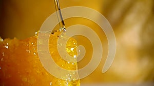 Honey dripping from honey dipper on honeycomb, over yellow background