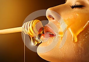 Honey dripping from honey dipper on sexy girl lips. Thick honey dipping from the wooden honey spoon. Beauty model woman