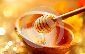 Honey dripping from honey dipper in wooden bowl.  Close-up. Healthy organic Thick honey dipping from the wooden honey spoon