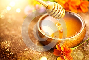 Honey dripping from honey dipper in wooden bowl.  Close-up. Healthy organic Thick honey dipping from the wooden honey spoon