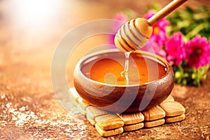 Honey dripping from honey dipper in wooden bowl.  Close-up. Healthy organic thick honey dipping from the wooden honey spoon